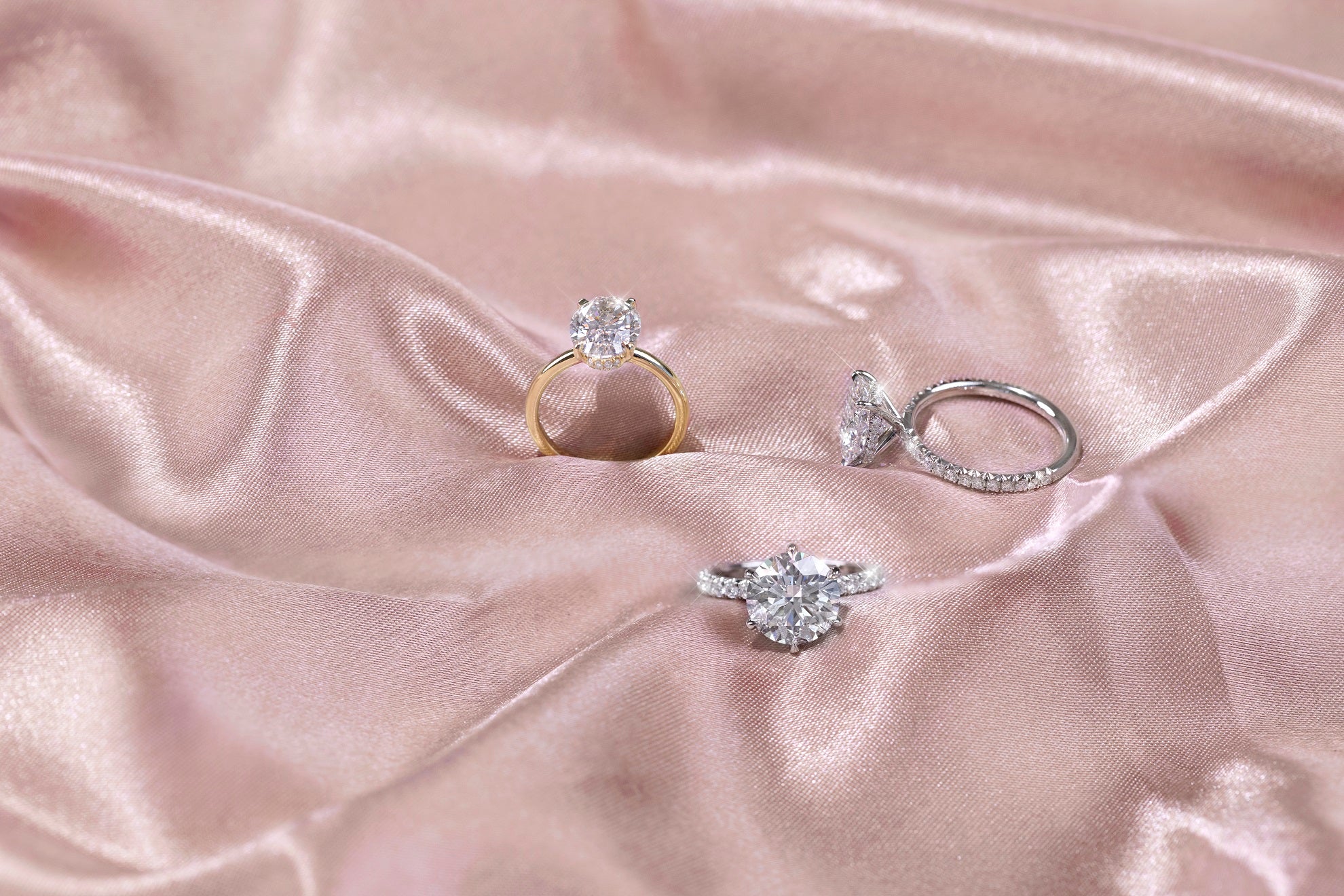 Three stunning engagement ring options: platinum round-cut with French pavé, oval-cut with French pavé and hidden halo, and two-tone oval-cut yellow gold with platinum prongs and hidden halo