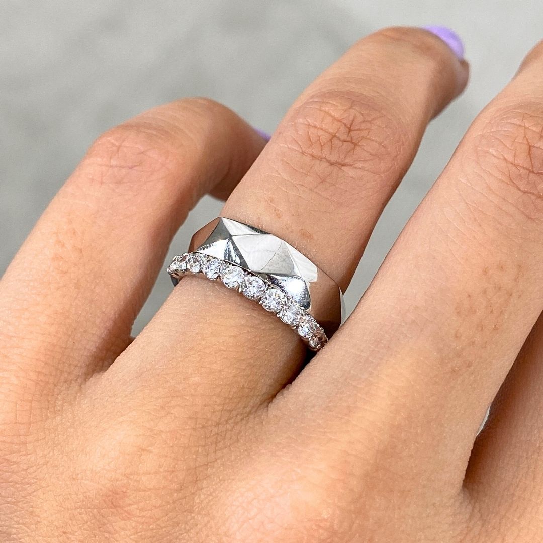 Silver ring with diamonds on a finger against a neutral background